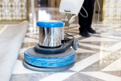 Person polishing a patterned tile floor with a floor buffing machine indoors